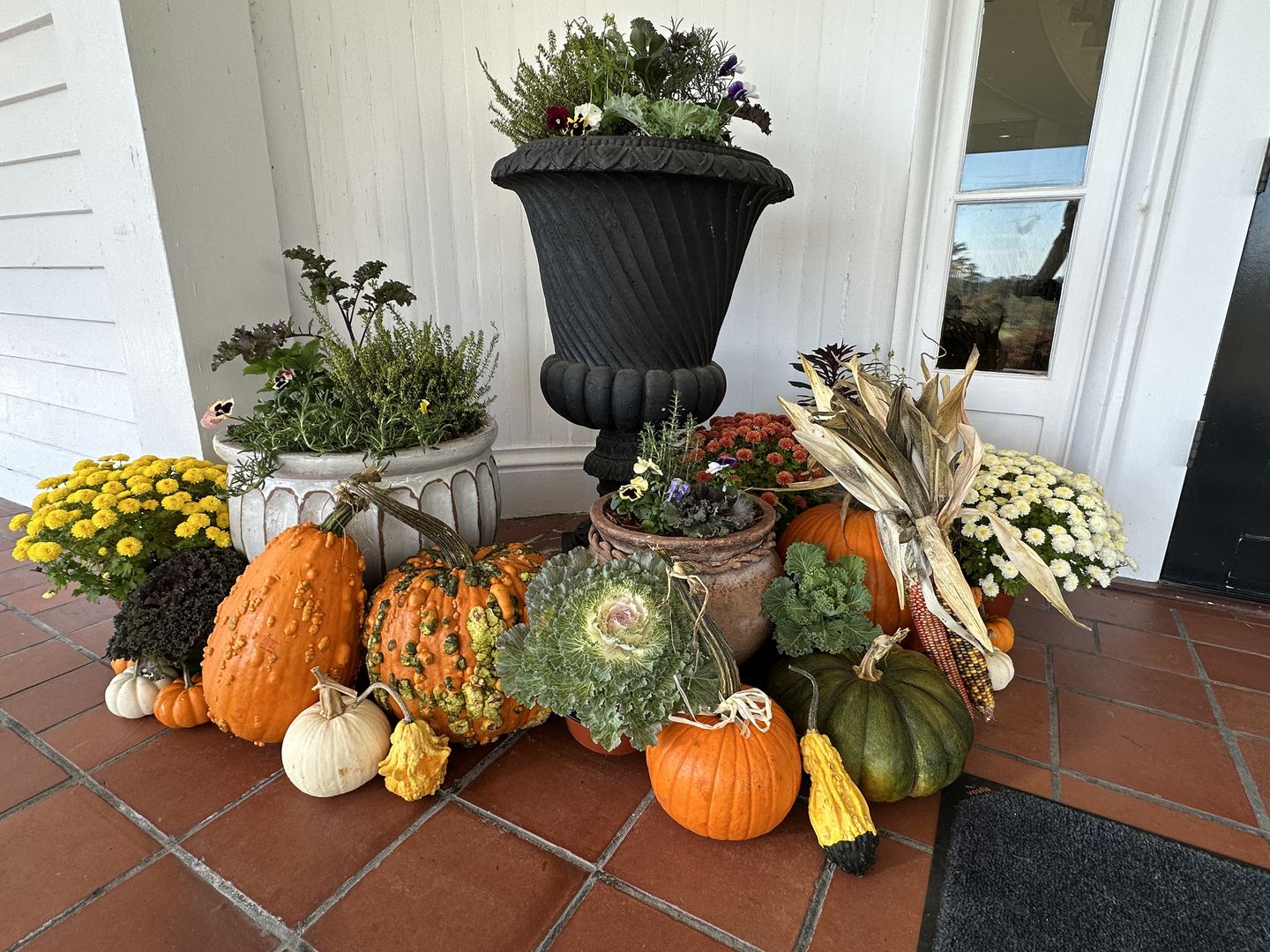 Fall front door styled with cool-season planters, ornamental cabbage, mums, pumpkins, and gourds