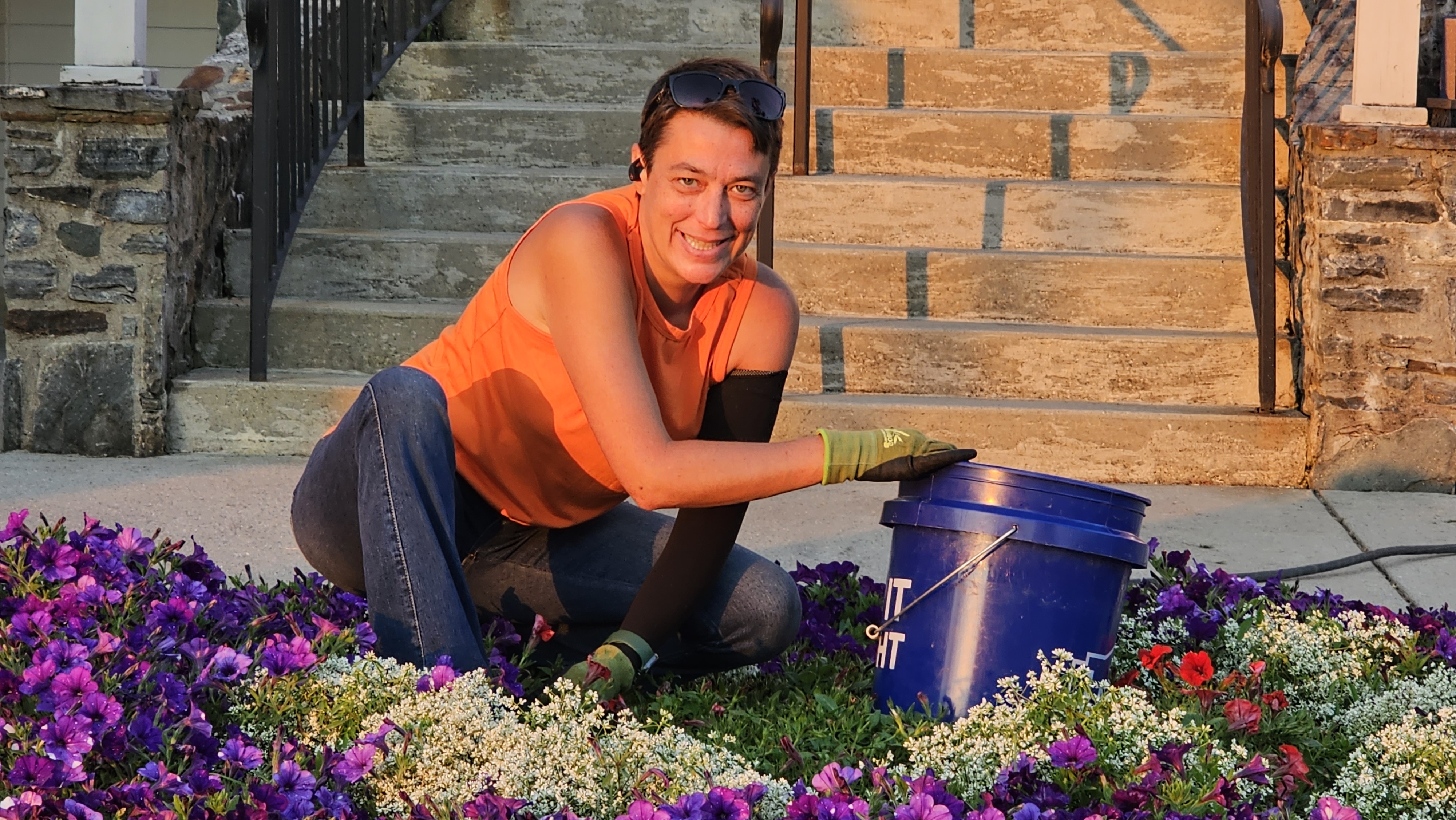 Holly working among purple and white flowers with her gardening gloves and planting bucket