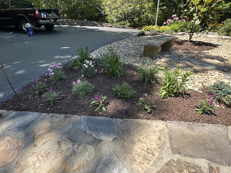Freshly mulched driveway bed with young plants and stone edging
